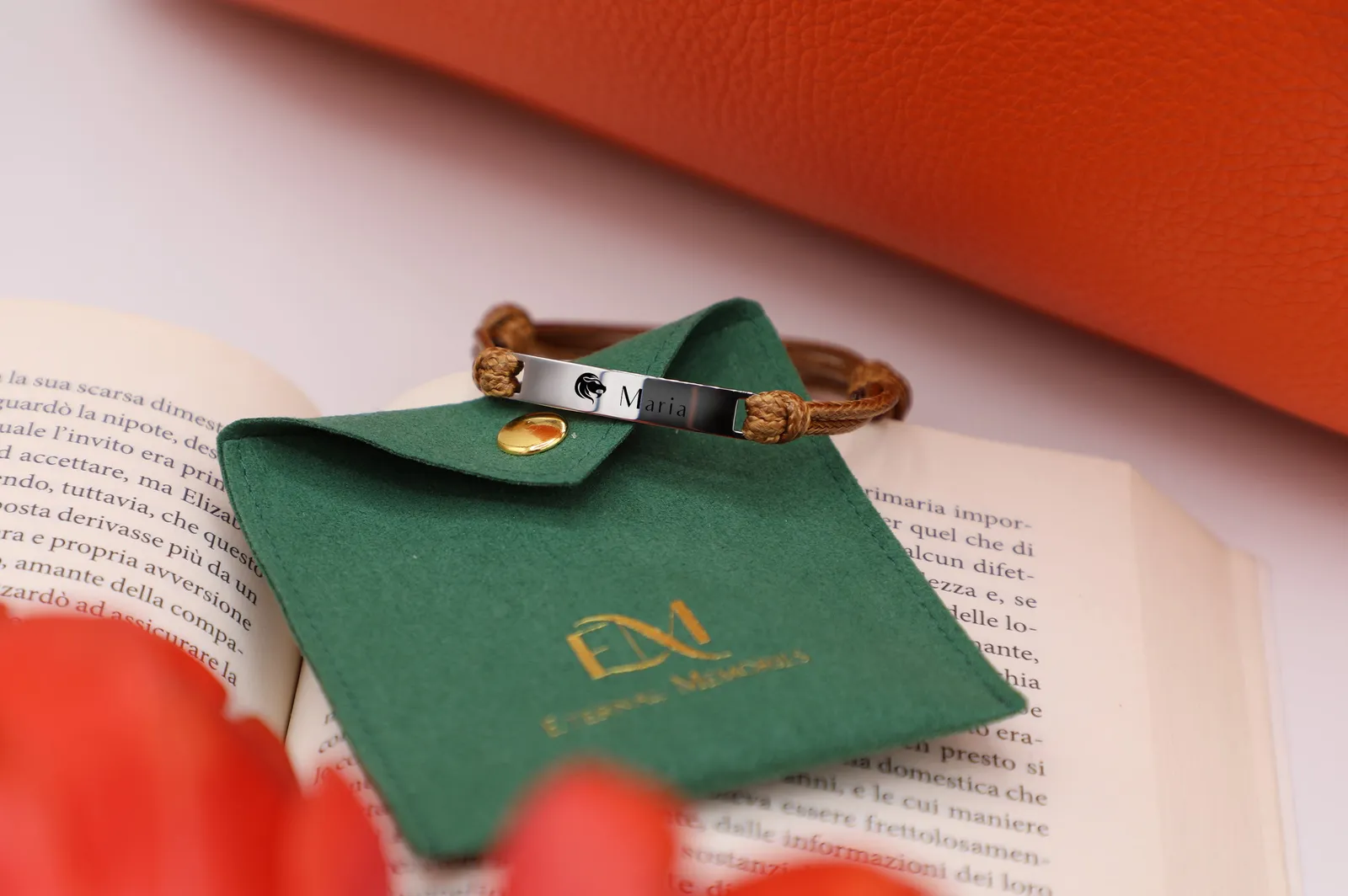 Bracciale inciso appoggiato sulla pochette verde con il logo dorato