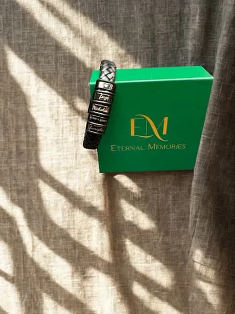 Bracciale in pelle nera con placche incise con nomi, sulla scatola verde Eternal Memories